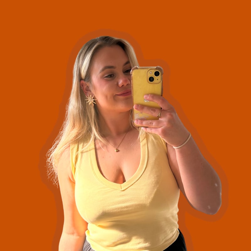 Amelia Marsh taking a mirror selfie with a yellow phone, in a yellow top, cut out on orange.