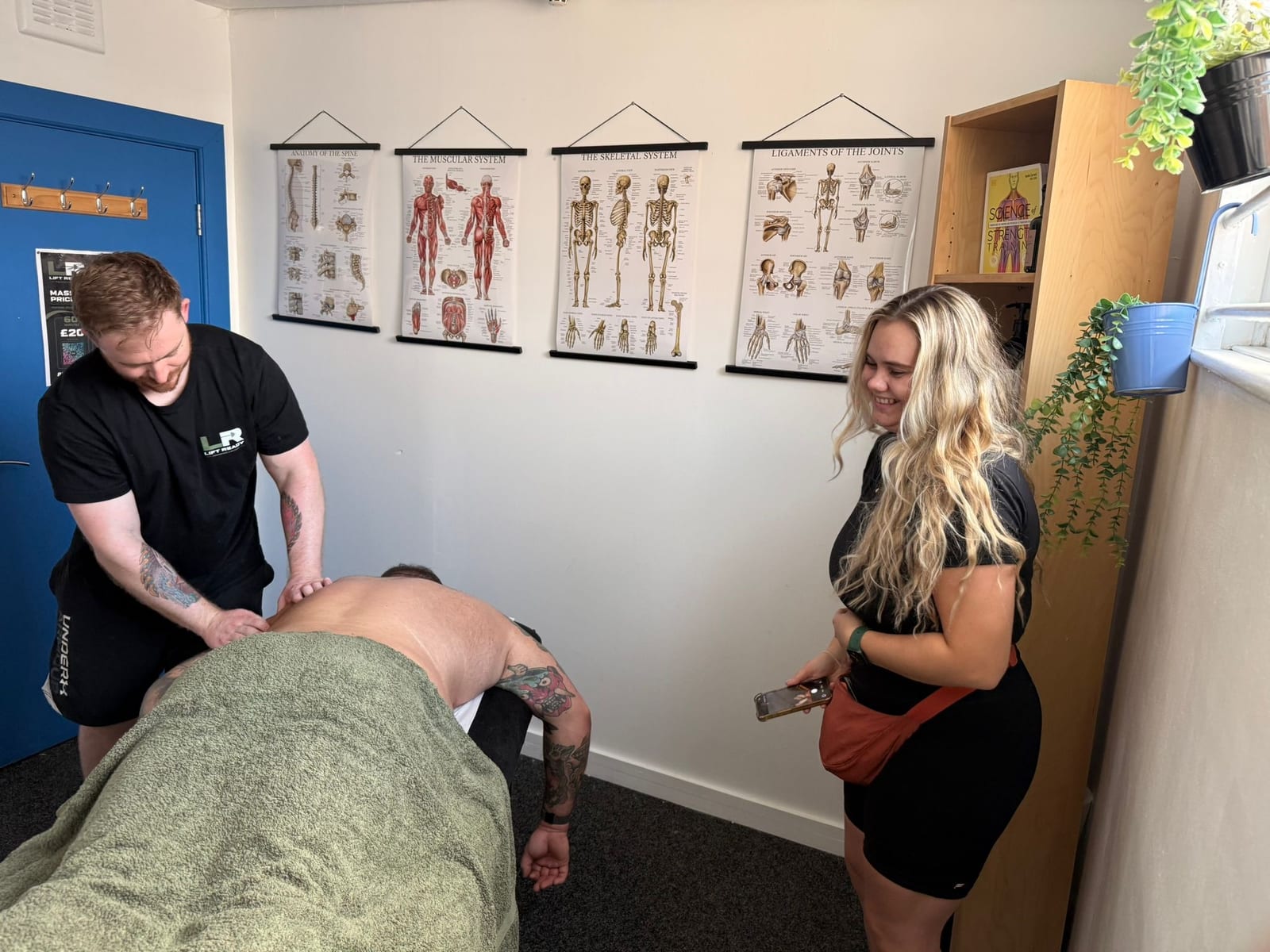 Amelia, phone in hand, watching a Lift Ready therapist work on a client.